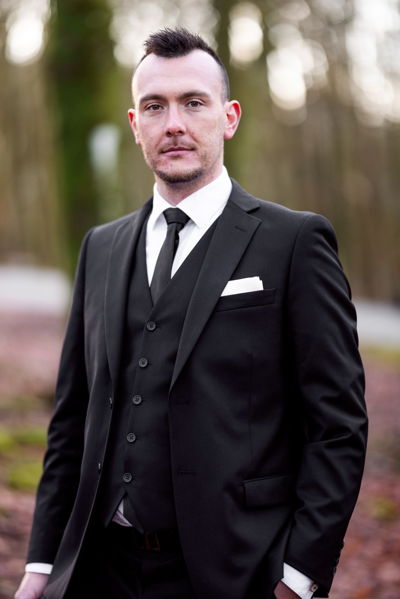 En mann i dress står utendørs med et seriøst uttrykk.